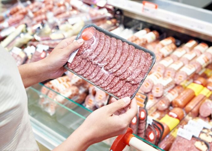 Photo shows someone holding up a package of highly processed red meat slices in the supermarket