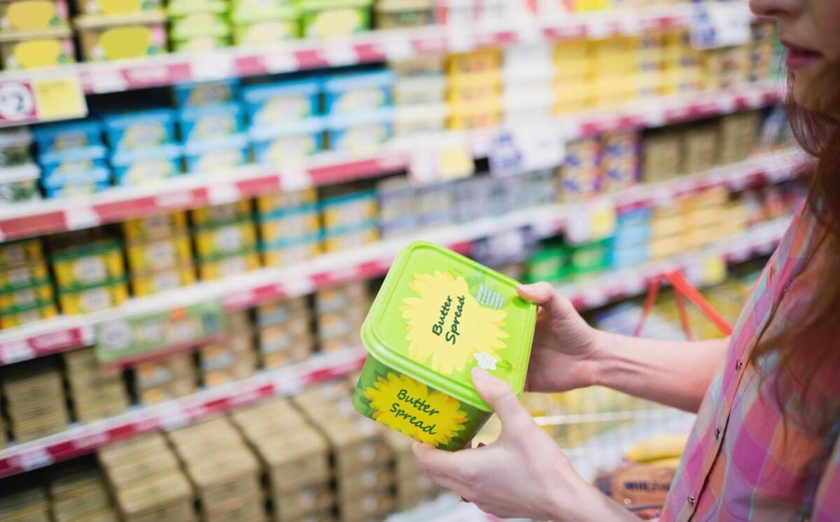 Photo shows a woman holding up a tub of butter-style margarine spread in a supermarket