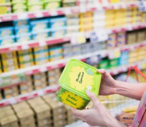 Photo shows a woman holding up a tub of butter-style margarine spread in a supermarket