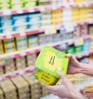 Photo shows a woman holding up a tub of butter-style margarine spread in a supermarket