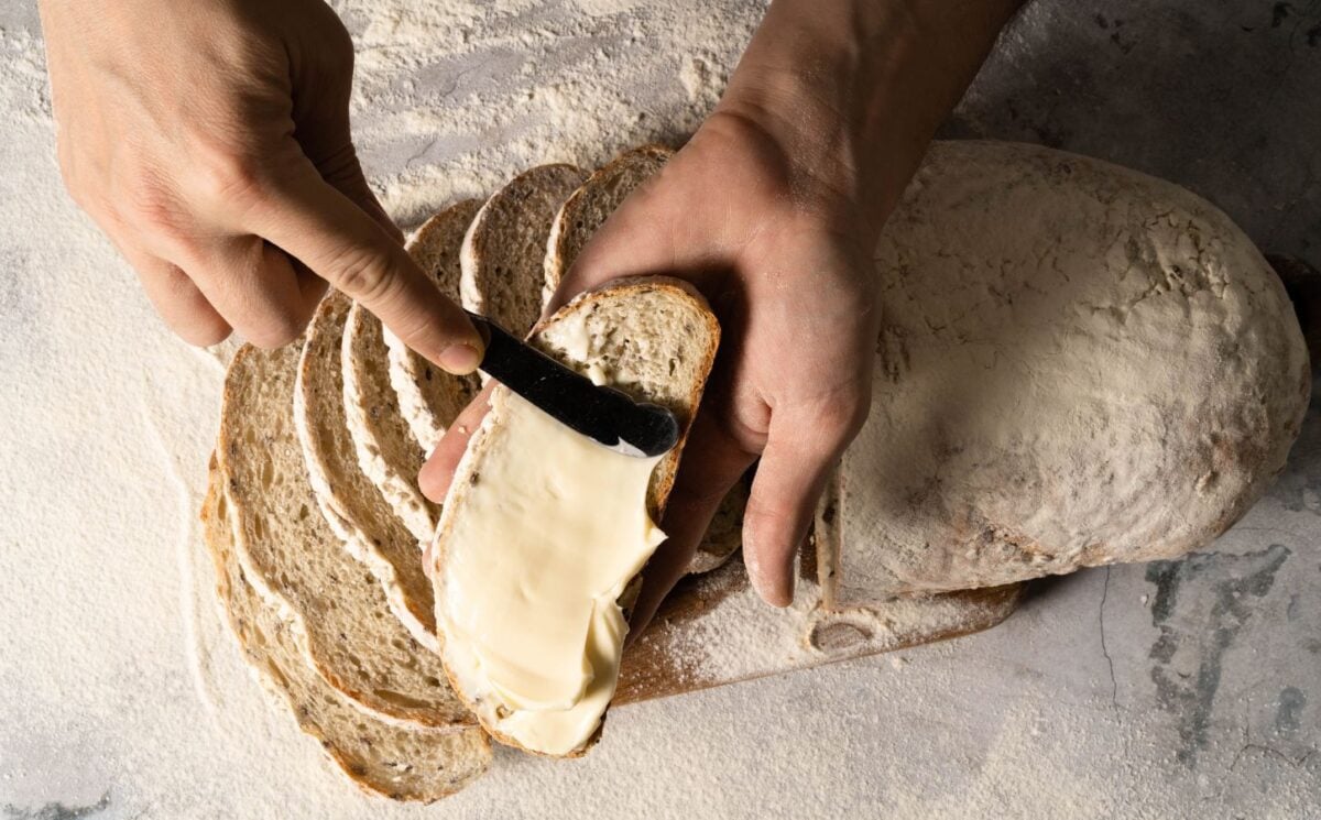 Photo shows someone's hands as they spread margarine on a slice of bread