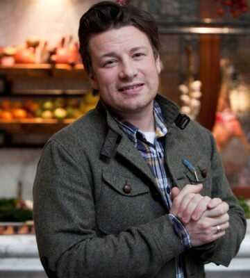 Photo shows Jamie Oliver standing in front of a kitchen stocked with fresh fruit and vegetables