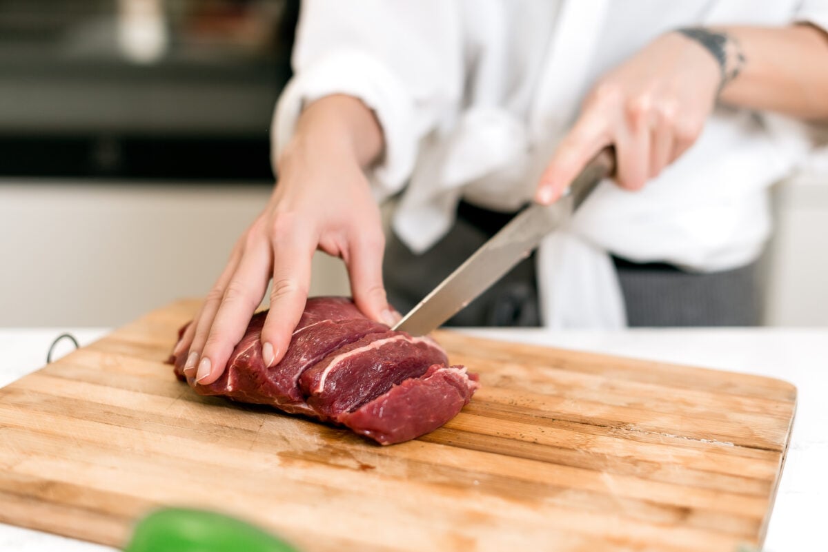 Photo shows a woman's hands as she cuts up a piece of red meat