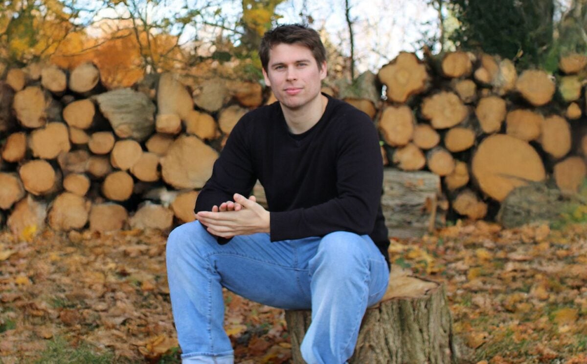 Plant Based News founder Klaus Mitchell sitting in some woods in front of some logs