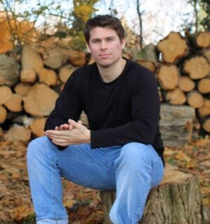Plant Based News founder Klaus Mitchell sitting in some woods in front of some logs