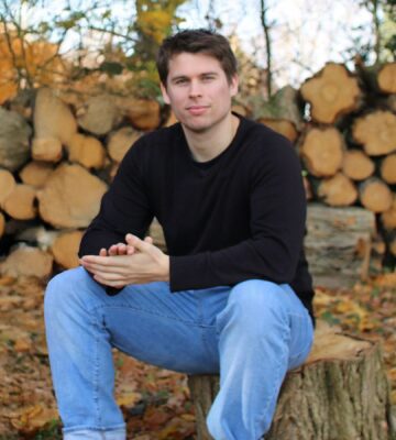 Plant Based News founder Klaus Mitchell sitting in some woods in front of some logs