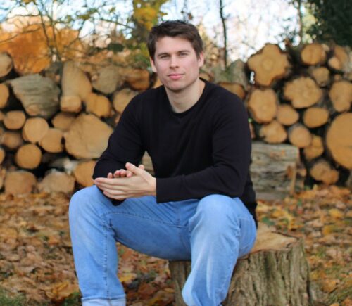 Plant Based News founder Klaus Mitchell sitting in some woods in front of some logs