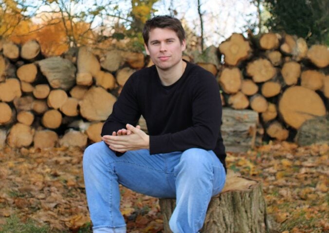 Plant Based News founder Klaus Mitchell sitting in some woods in front of some logs