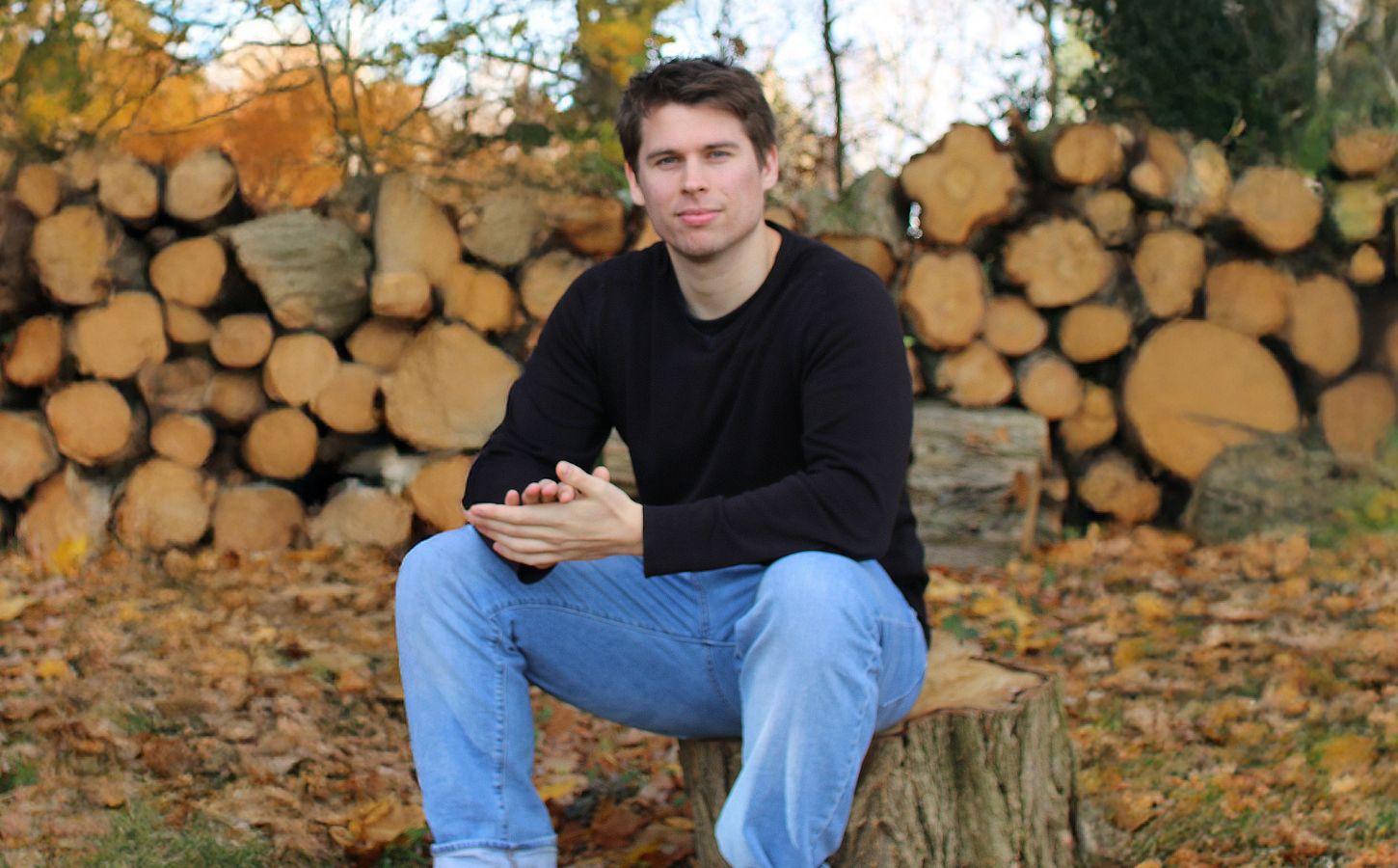 Plant Based News founder Klaus Mitchell sitting in some woods in front of some logs