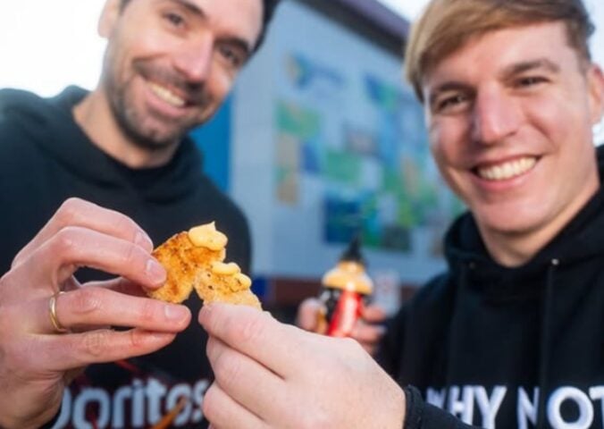Photo shows two men in Doritos and NotCo branded sweatshirts holding Flamin' Hot flavored "NotChicken Nuggets" from the two brands