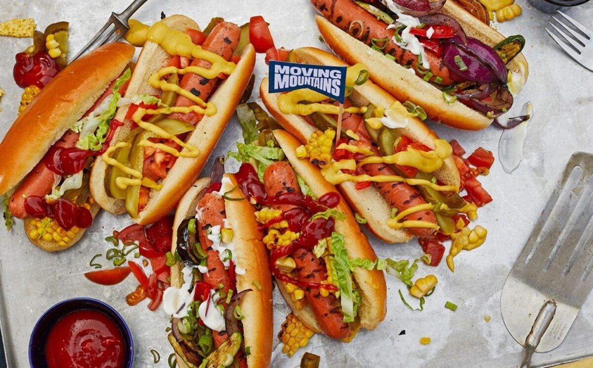 Photo shows a selection of vegan Moving Mountains hot dogs topped with pickles and sauce