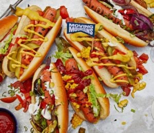 Photo shows a selection of vegan Moving Mountains hot dogs topped with pickles and sauce