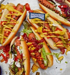Photo shows a selection of vegan Moving Mountains hot dogs topped with pickles and sauce