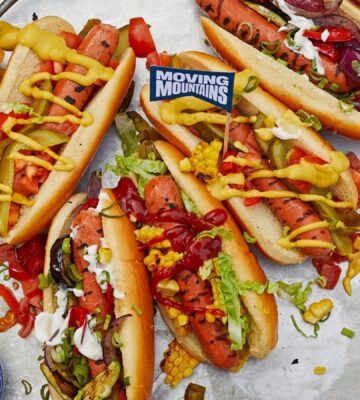 Photo shows a selection of vegan Moving Mountains hot dogs topped with pickles and sauce