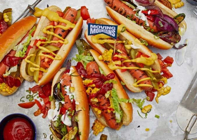 Photo shows a selection of vegan Moving Mountains hot dogs topped with pickles and sauce