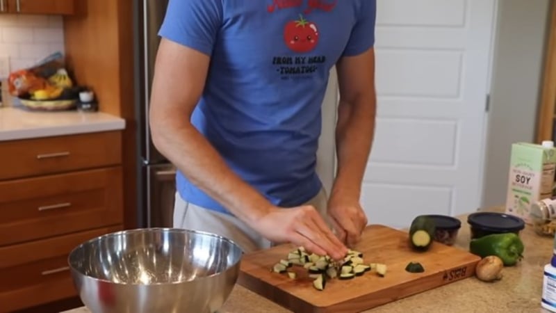 Dillon Holmes chops a courgette on a wooden chopping board in his kitchen as he makes a viral oatmeal pizza recipe