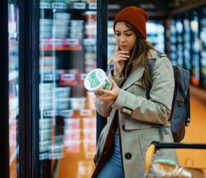 Photo shows a young woman reading the back of a dairy product in the supermarket