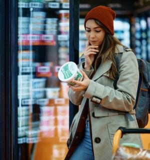 Photo shows a young woman reading the back of a dairy product in the supermarket