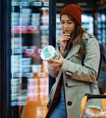 Photo shows a young woman reading the back of a dairy product in the supermarket