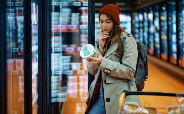 Photo shows a young woman reading the back of a dairy product in the supermarket