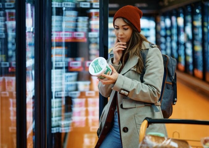 Photo shows a young woman reading the back of a dairy product in the supermarket
