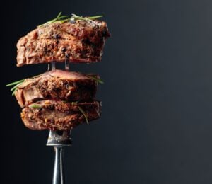 Photo shows a silver fork with several thick pieces of steak on it