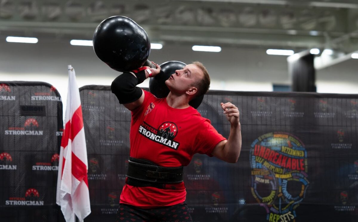 Photo shows vegan athlete Tom Butts lifting an 80kg strongman-style dumbbell