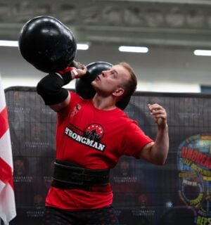 Photo shows vegan athlete Tom Butts lifting an 80kg strongman-style dumbbell