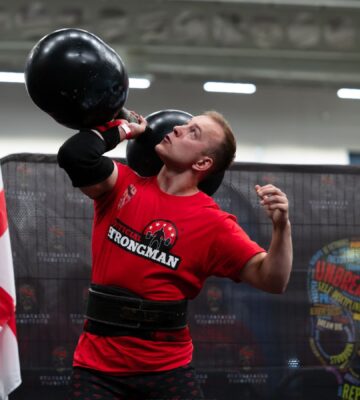 Photo shows vegan athlete Tom Butts lifting an 80kg strongman-style dumbbell