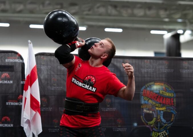 Photo shows vegan athlete Tom Butts lifting an 80kg strongman-style dumbbell