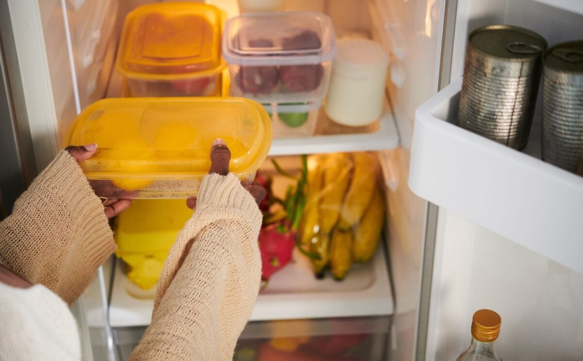A person putting a tupperware box in a fridge while setting up a vegan kitchen