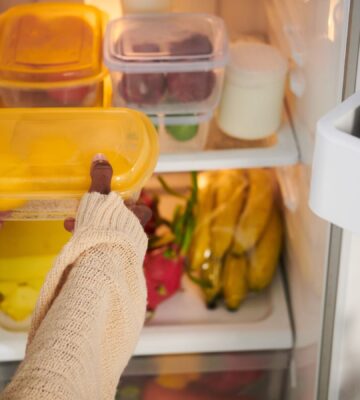 A person putting a tupperware box in a fridge while setting up a vegan kitchen