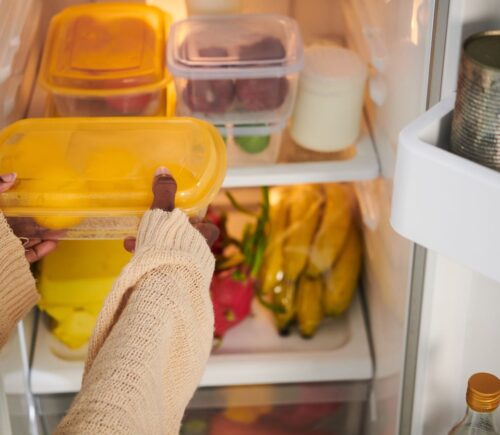 A person putting a tupperware box in a fridge while setting up a vegan kitchen