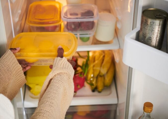 A person putting a tupperware box in a fridge while setting up a vegan kitchen
