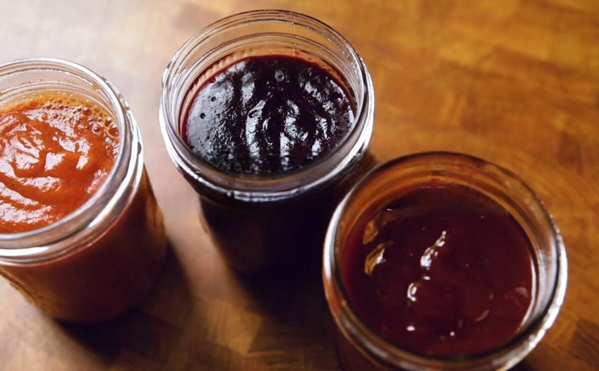 A shot of the three vegan bbq sauces, classic, blueberry, and peach habanero, all lined up in glass jam jars