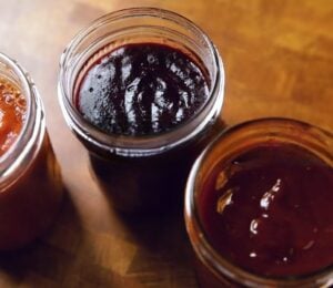 A shot of the three vegan bbq sauces, classic, blueberry, and peach habanero, all lined up in glass jam jars