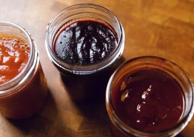 A shot of the three vegan bbq sauces, classic, blueberry, and peach habanero, all lined up in glass jam jars