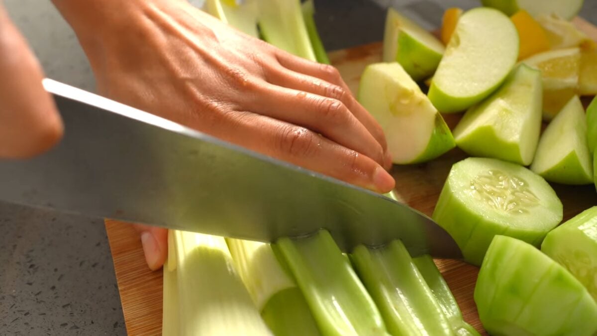 Reyes chops a bunch of celery on a chopping board next to sliced cucumber, apples, and lemon, to prep her favorite iron-rich green juice