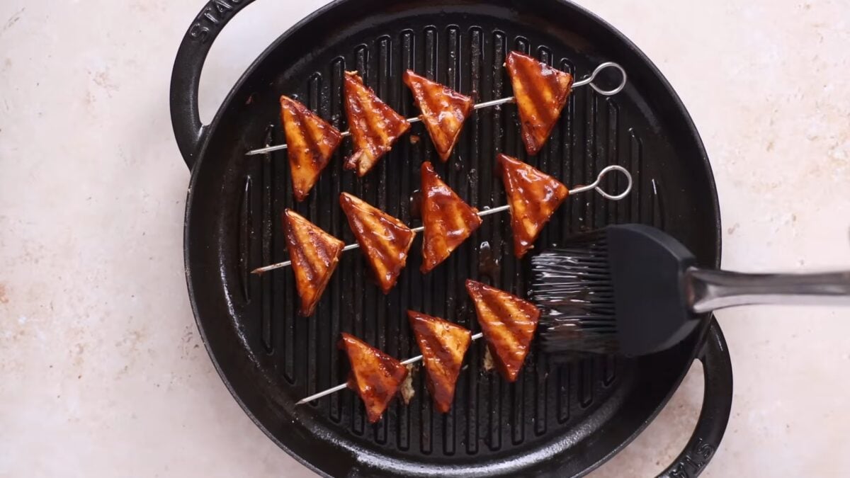Claiborne brushes the tofu with bbq sauce while grilling it in her video on easy vegan meal prep for back-to-school season