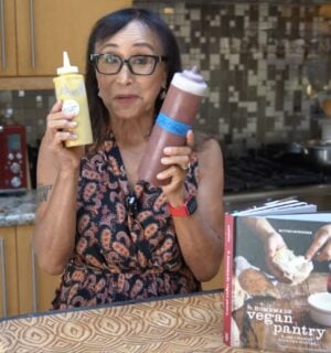 Miyoko Schinner stands in her kitchen holding two squeeze bottles of her homemade vegan ketchup and mustard