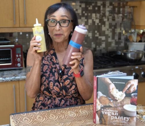 Miyoko Schinner stands in her kitchen holding two squeeze bottles of her homemade vegan ketchup and mustard