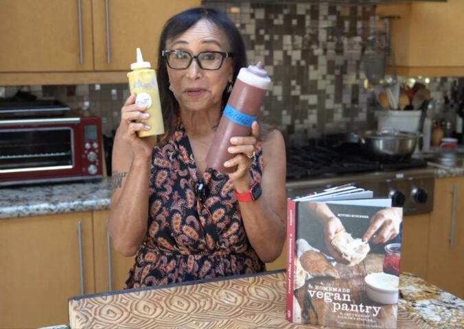 Miyoko Schinner stands in her kitchen holding two squeeze bottles of her homemade vegan ketchup and mustard