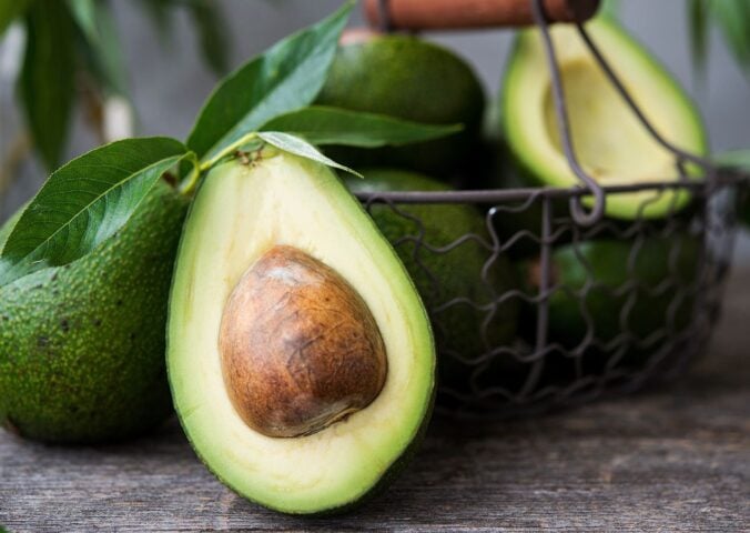 A basket of avocados, including a close-up of an avocado half
