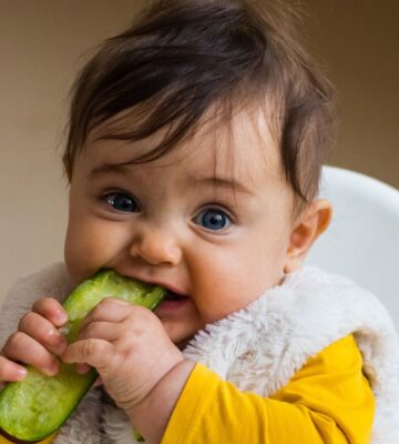 Photo shows a baby eating a slice of cucumber or pickle