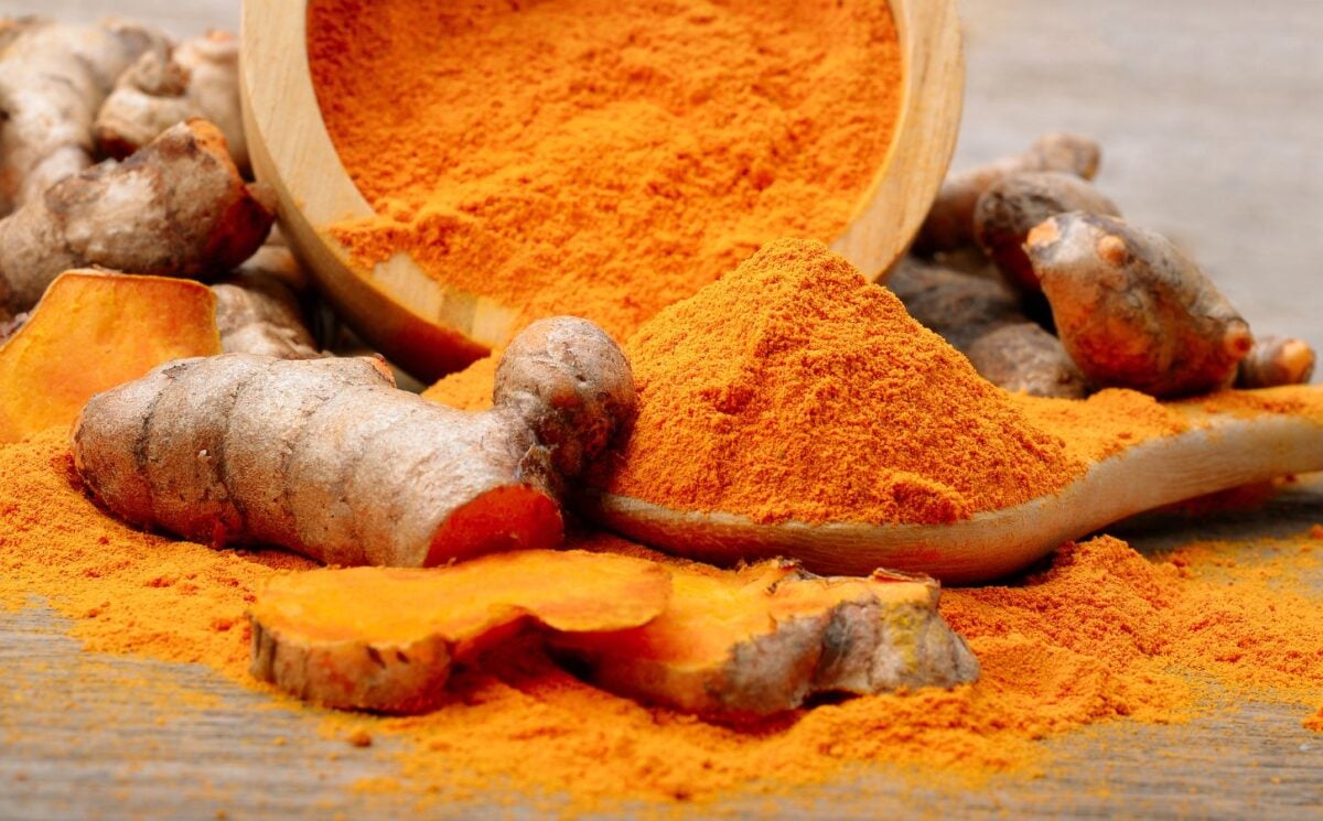 Powdered turmeric next to a turmeric root on a table