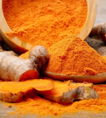 Powdered turmeric next to a turmeric root on a table