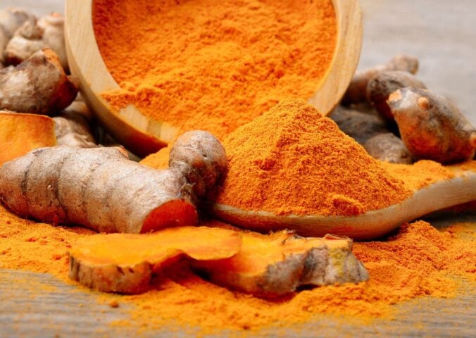 Powdered turmeric next to a turmeric root on a table