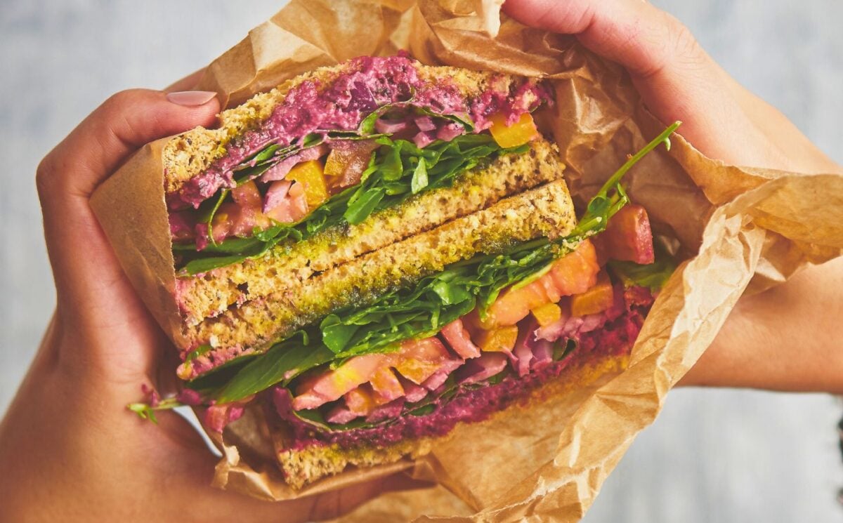 an epic veggie sandwich with red onion, tomato, yellow bell pepper, and more for vegan lunchbox ideas kids will love