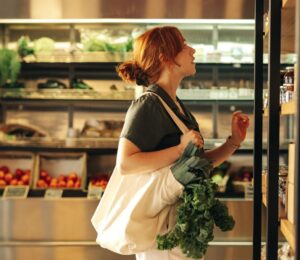 Photo shows a young woman with green leafy vegetables in her bag shopping at a supermarket