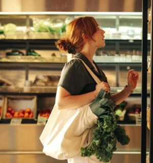 Photo shows a young woman with green leafy vegetables in her bag shopping at a supermarket